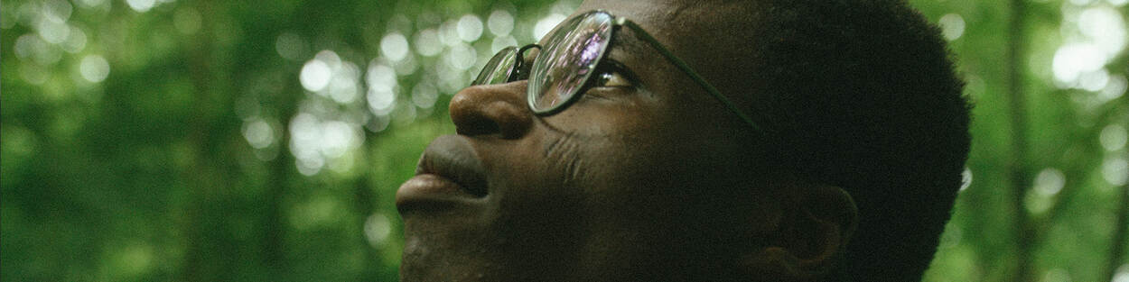 Portret van een donkere man met bril die omhoog kijkt in het bos