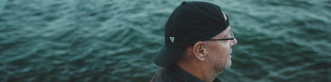 Oudere man met pet achterop zijn hoofd kijk richting zee